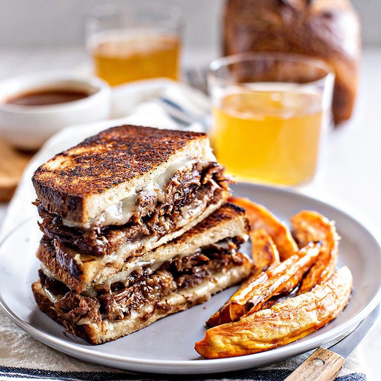 photo of a french dip panini on a plate with sweet potato fries and a glass of beer
