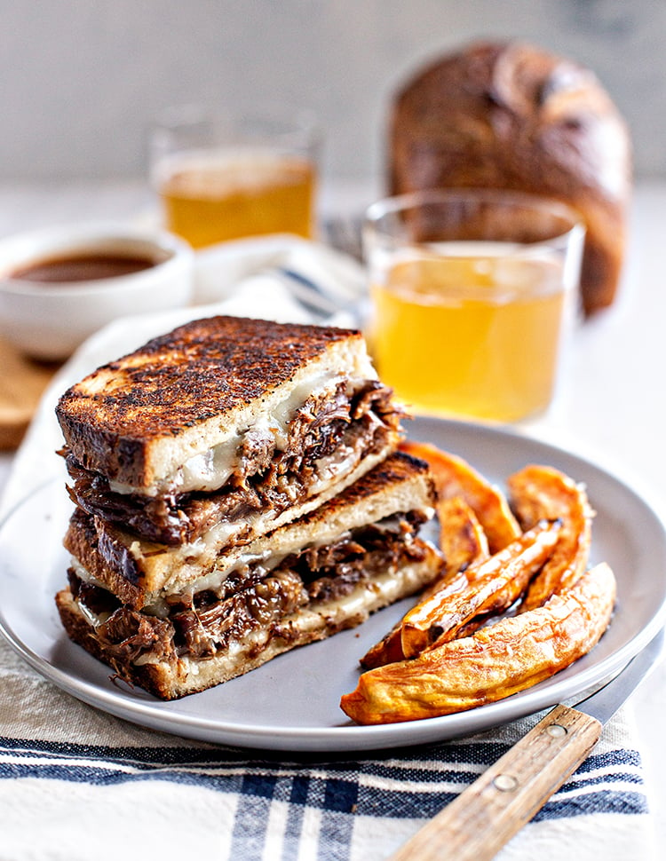 photo of a french dip panini on a plate with sweet potato fries and a glass of beer