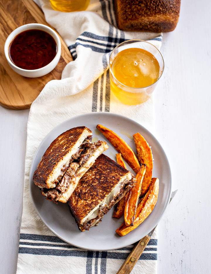 photo of french dip panini on a plate with sweet potato fries and a glass of beer