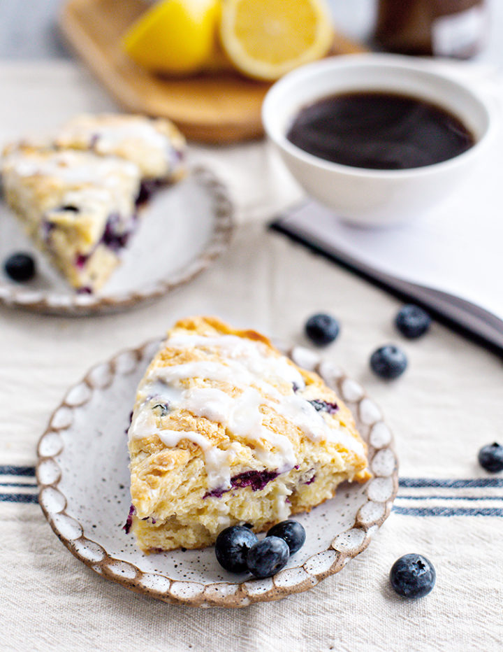 photo of blueberry lemon scones on plate with a mug of coffee and a book