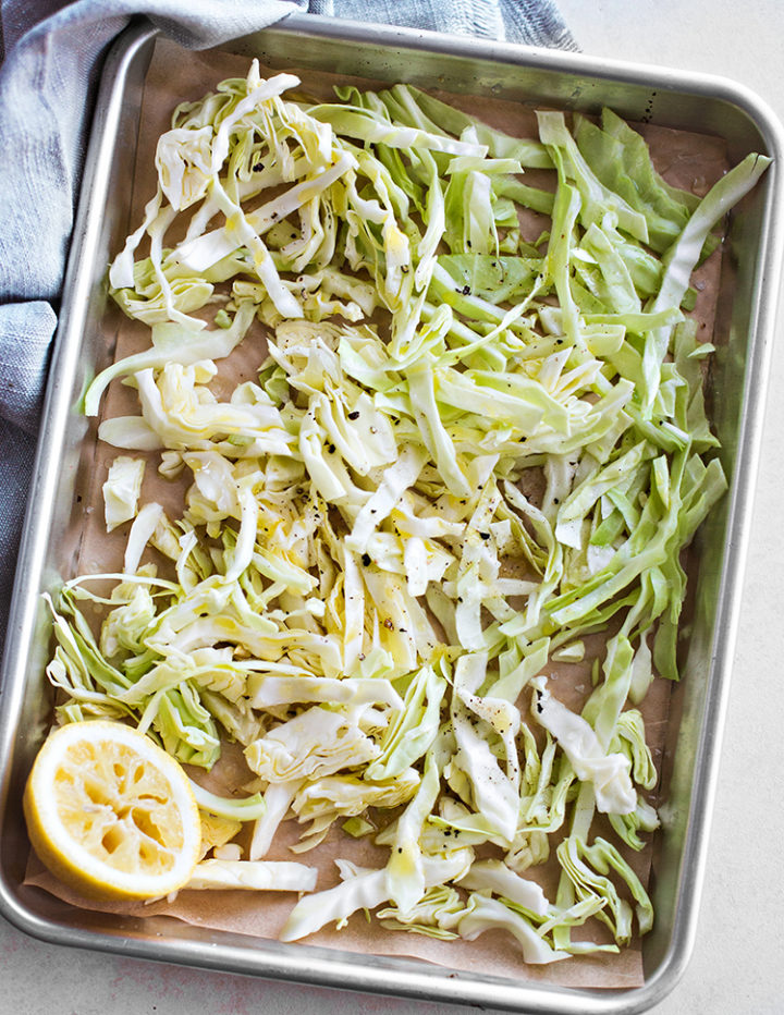 overhead shot of shredded cabbage with lemon on a parchment lined sheet pan