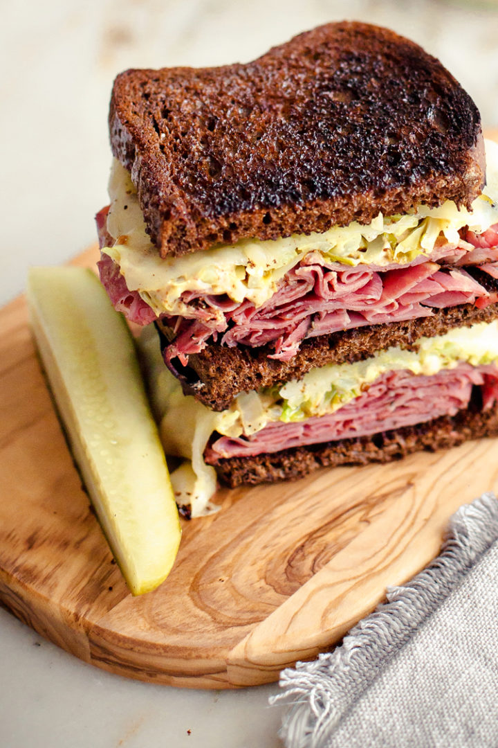 close up shot of a reuben sandwich using leftover corned beef on a cutting board with a pickle