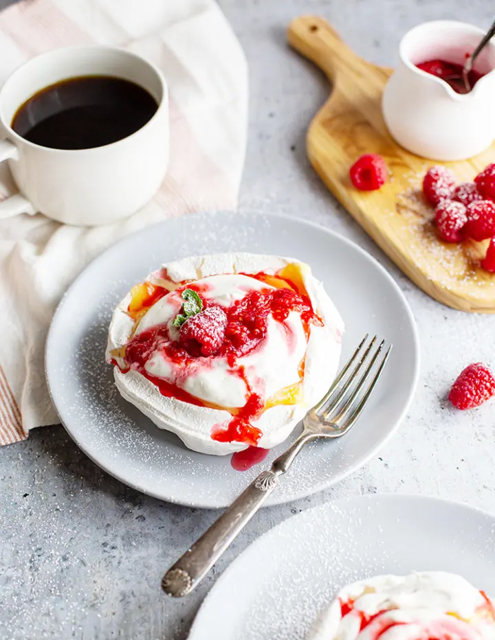photo of a pavlova dessert with lemon curd and raspberries on a plate with fresh raspberries