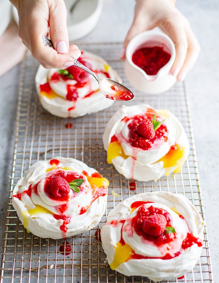 photo of woman spooning raspberry sauce on a lemon curd pavlova dessert