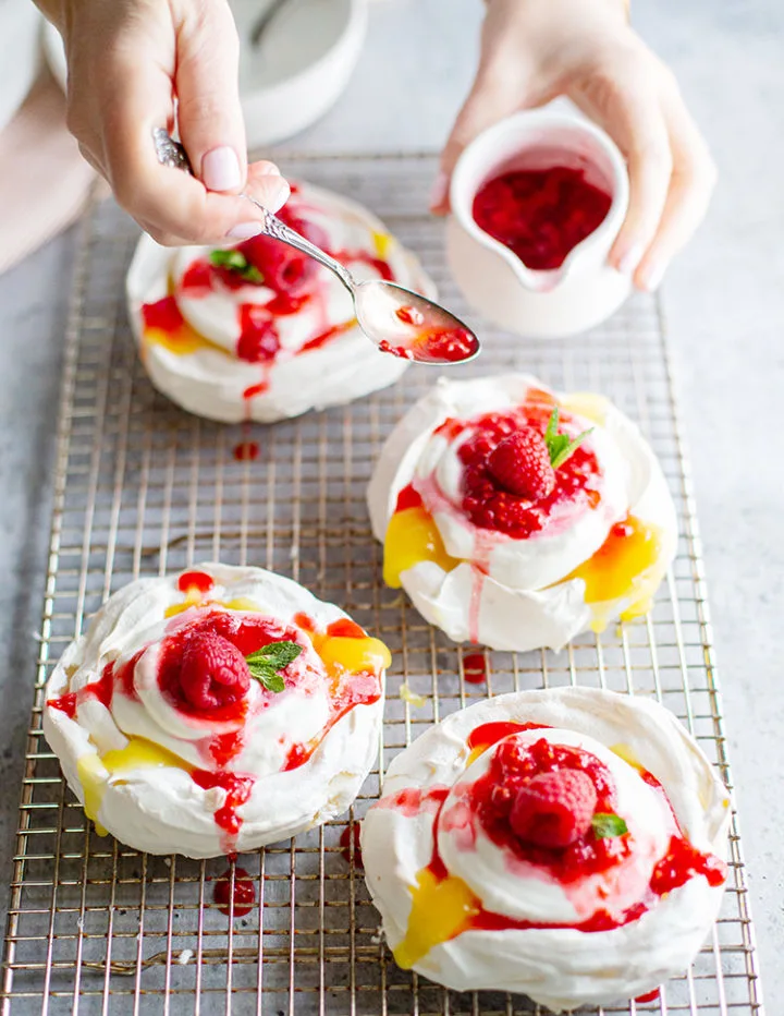 photo of woman spooning raspberry sauce on a lemon curd pavlova dessert