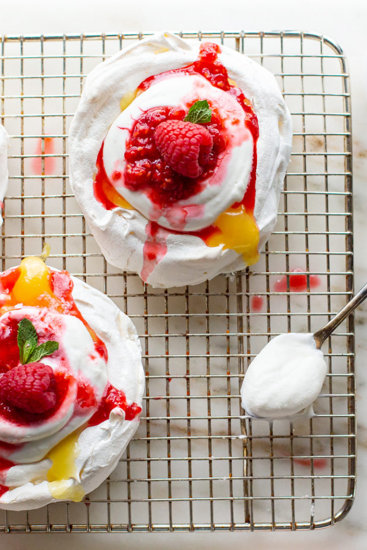 overhead shot of pavlova dessert with lemon curd, whipped cream, and raspberries