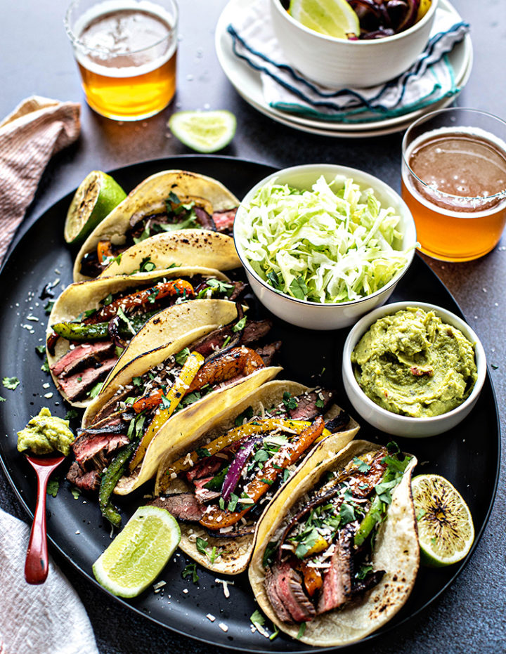 photo of a platter of flank steak fajitas with lettuce, guacamole, and glasses of beer