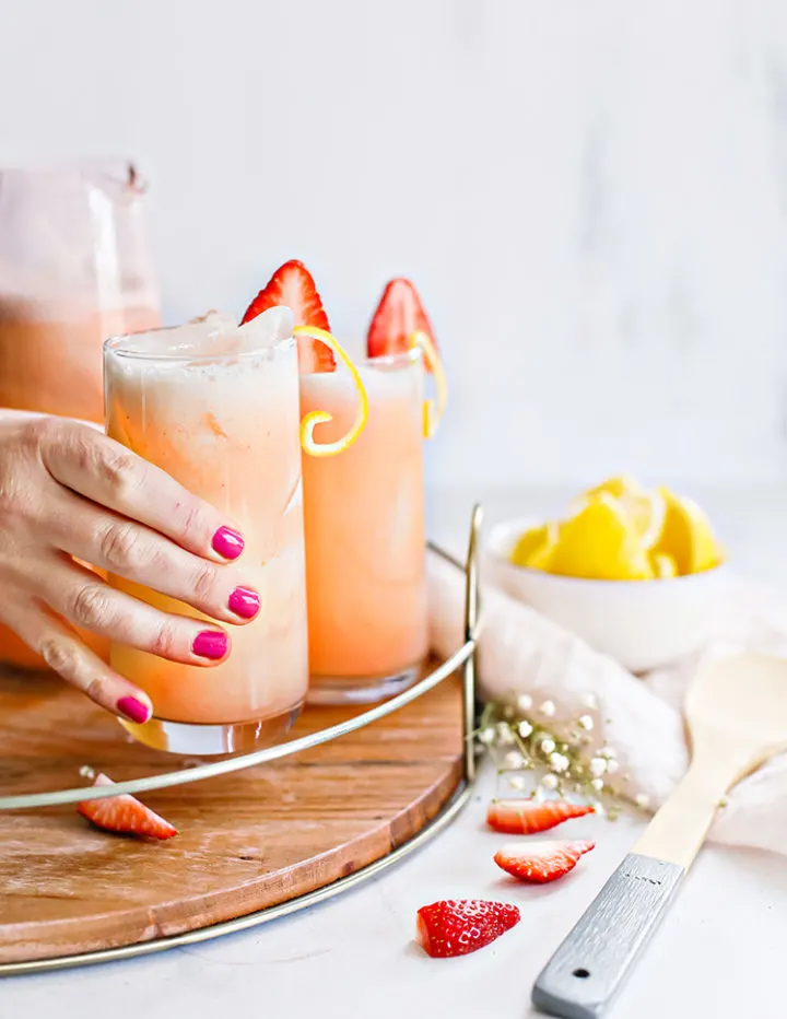 strawberrylemonaderecipe photo of a woman's hand placing a glass of fresh strawberry lemonade on a drink tray