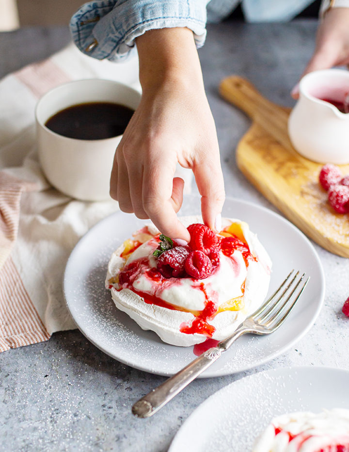 photo of woman placing fresh raspberries on a lemon curd pavlova dessert