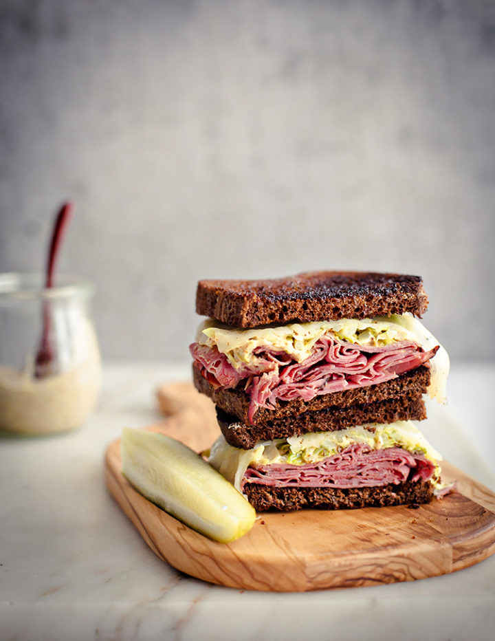 reuben sandwich using leftover corned beef on a cutting board with a pickle