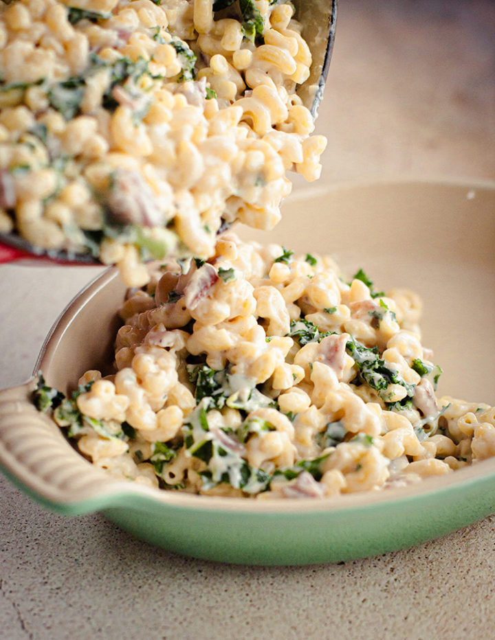 pouring White Cheddar Mac and Cheese with kale and bacon into a casserole dish before baking