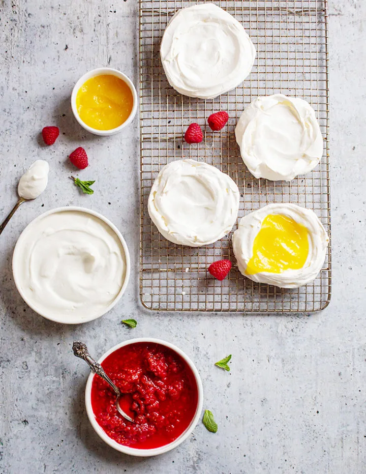 a photo of pavlova dessert ingredients: meringue shells, lemon curd, whipped cream, and raspberry sauce