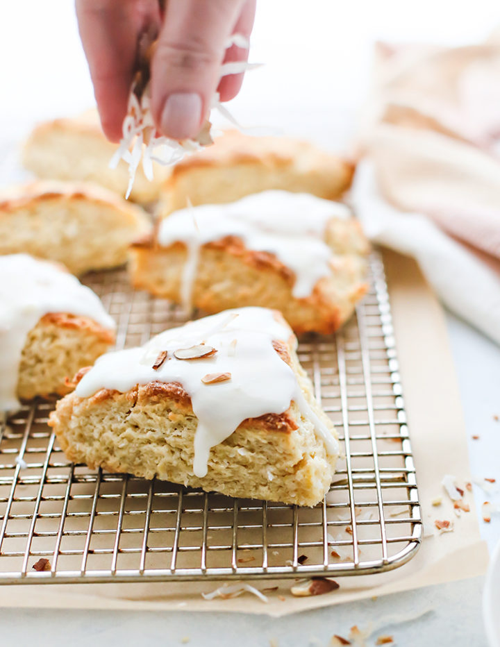 photo of hands sprinkling toasted coconut and almonds on top of glazed coconut scones