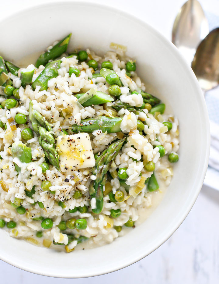 Close-up of creamy lemon asparagus risotto in a white bowl, filled with vibrant peas, sliced asparagus, and leeks. Topped with a pat of butter, lemon zest, and cracked pepper, this spring risotto looks warm, comforting, and fresh from the stove.