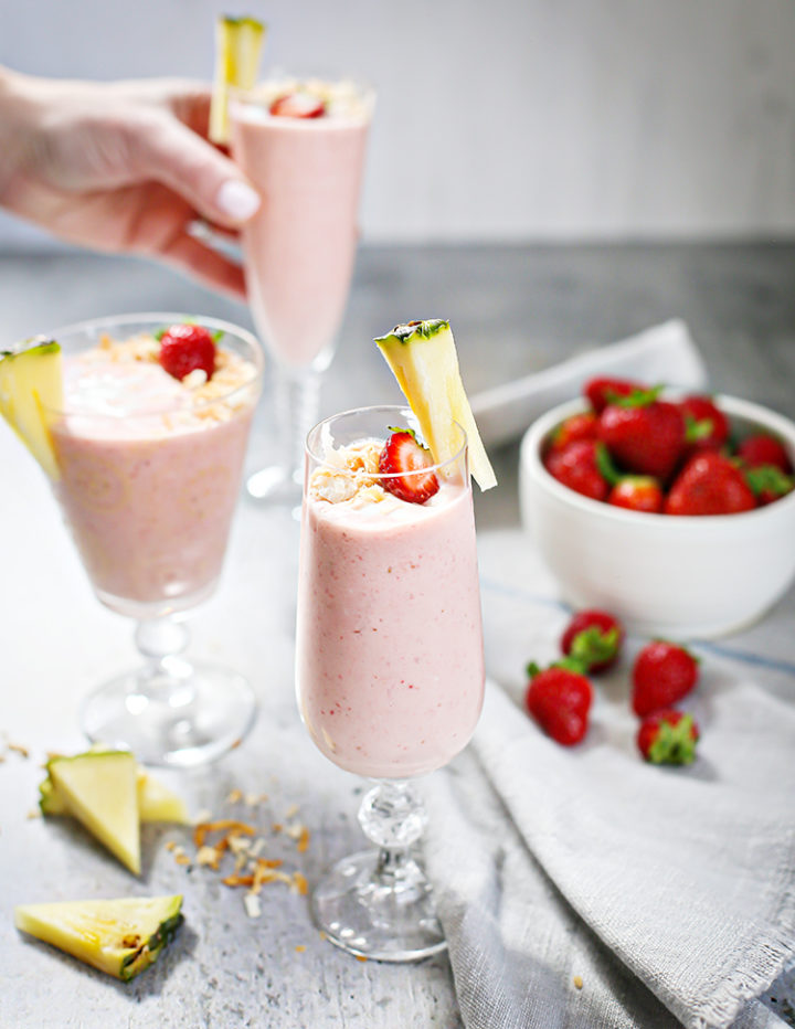 woman setting 3 glasses of Strawberry Pineapple Smoothie on a table next to a bowl of strawberries