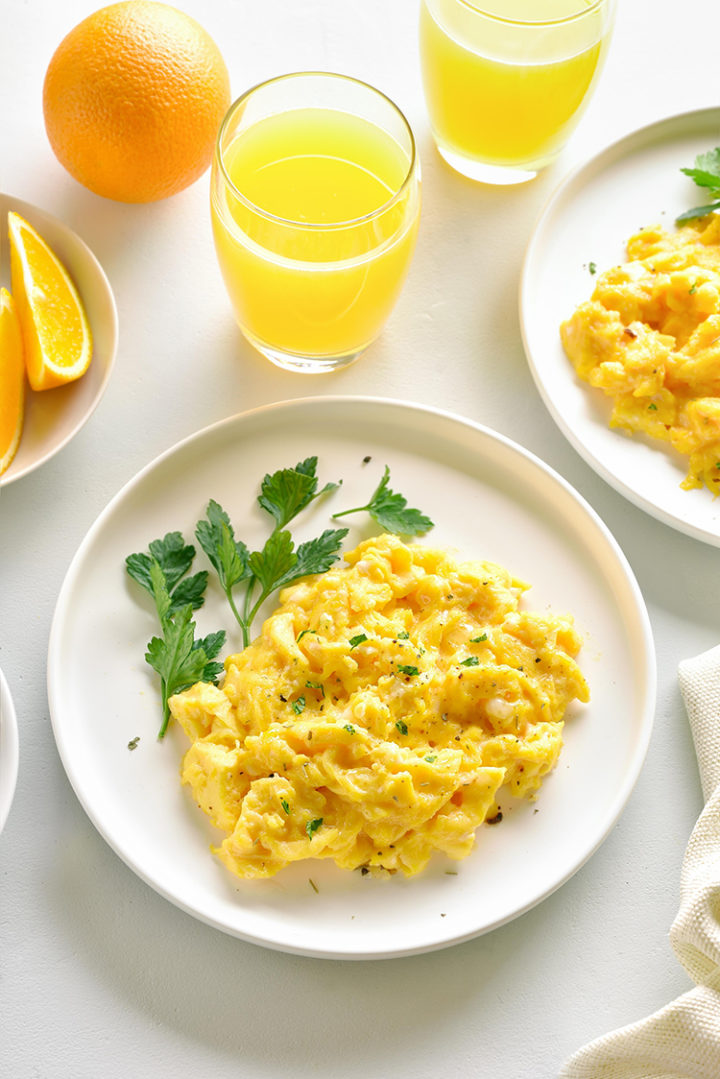 a photo of a white plate with scrambled eggs on a table with orange juice in glasses