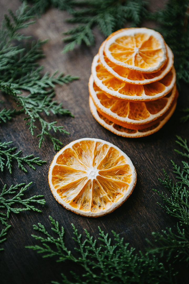 photo of dried orange slices on a wooden table with greenery surrounding them