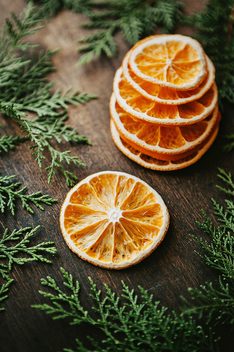 a stack of dried orange slices on a wooden table with greenery around them
