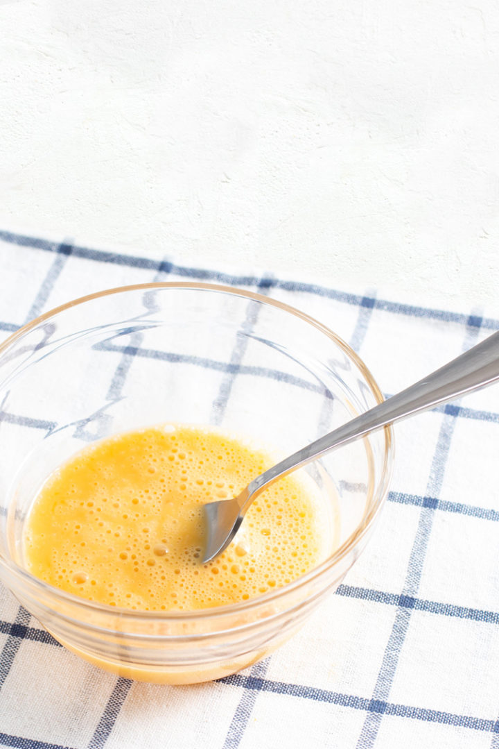 a photo of eggs in a glass bowl with a fork being beaten to make scrambled eggs