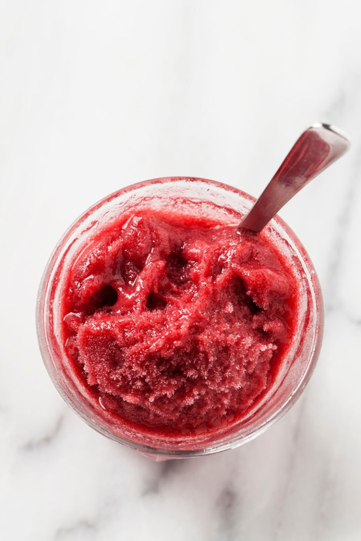 overhead photo of pomegranate sorbet in a glass with a spoon