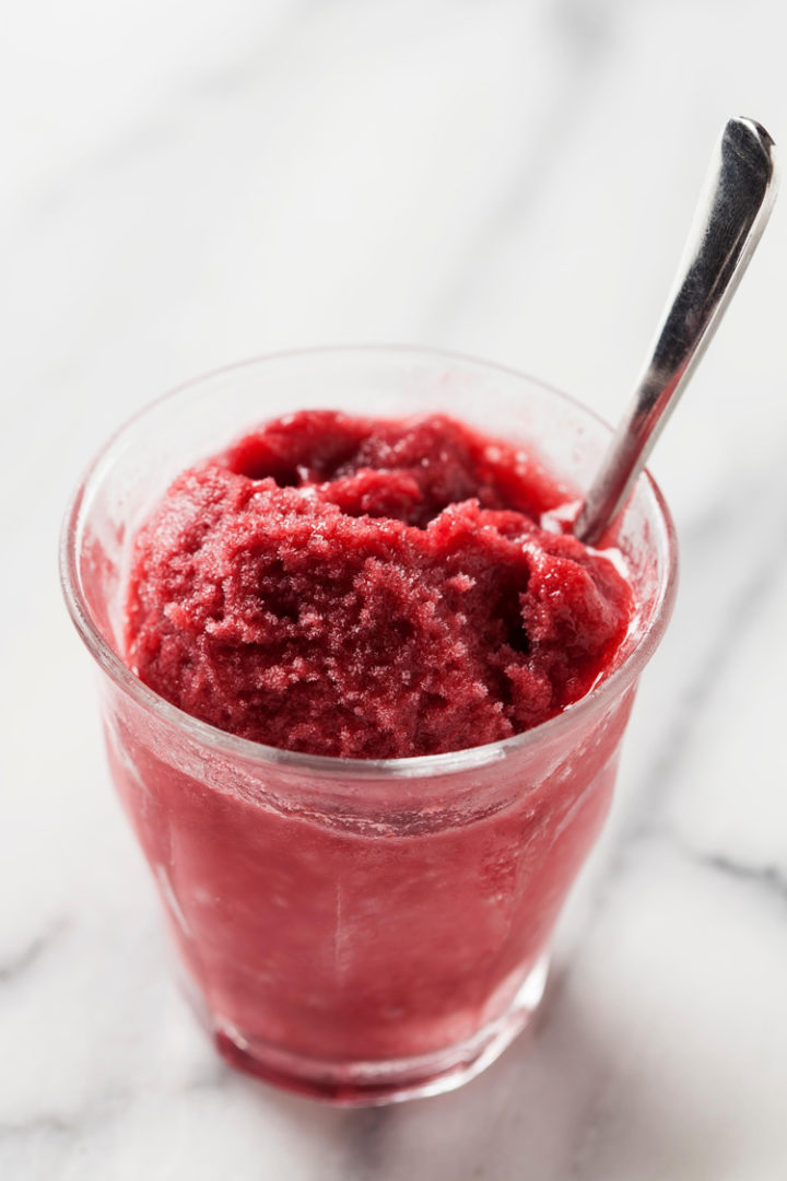 close up photo of a single glass of pomegranate sorbet on a marble counter