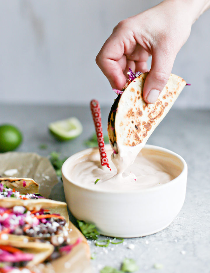 photo of woman dipping black bean tacos into crema