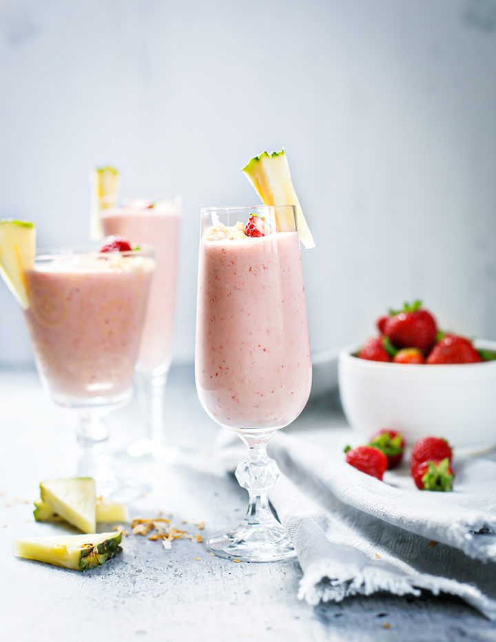 photo of 3 glasses of Strawberry Pineapple Smoothie next to a bowl of strawberries