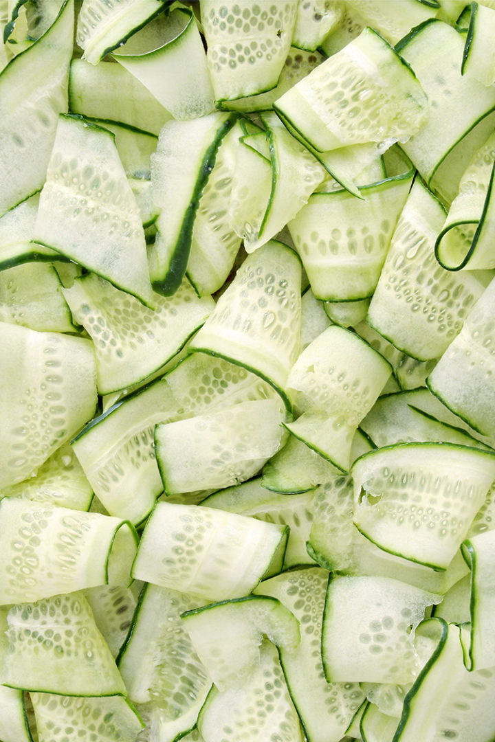 close up overhead photo of thin strips of cucumber for a cucumber spa water recipe #infusedwater #cucumberwater #mintwater #cucumbermintwater #cucumberandmintwater #freshcucumberwater #cucumberwaterrecipe #spawater #detoxwater #waterinfusedwithcucumber #herbwater