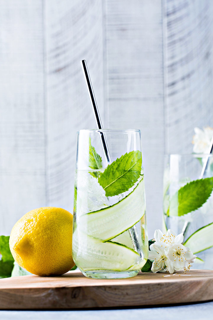 photo of a glass of cucumber mint water on a wooden cutting board next to a fresh lemon #infusedwater #cucumberwater #mintwater #cucumbermintwater #cucumberandmintwater #freshcucumberwater #cucumberwaterrecipe #spawater #detoxwater #waterinfusedwithcucumber #herbwater