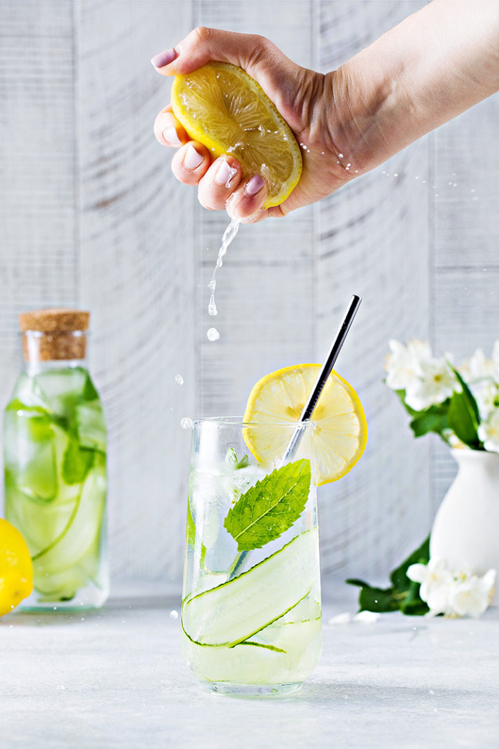 photo of a woman's hand squeezing a lemon into a glass of cucumber mint water #infusedwater #cucumberwater #mintwater #cucumbermintwater #cucumberandmintwater #freshcucumberwater #cucumberwaterrecipe #spawater #detoxwater #waterinfusedwithcucumber #herbwater