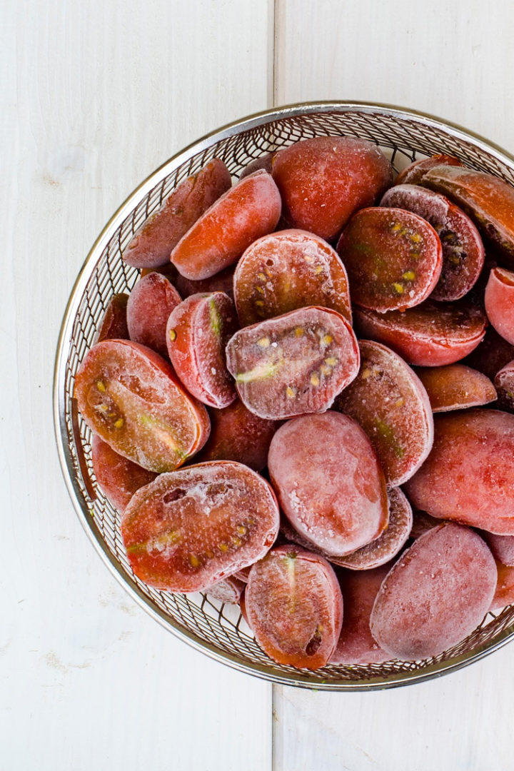 overhead photo of halved frozen tomatoes in a colander 