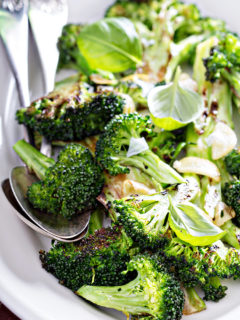 photo of roasted broccoli in a white serving dish with serving spoons