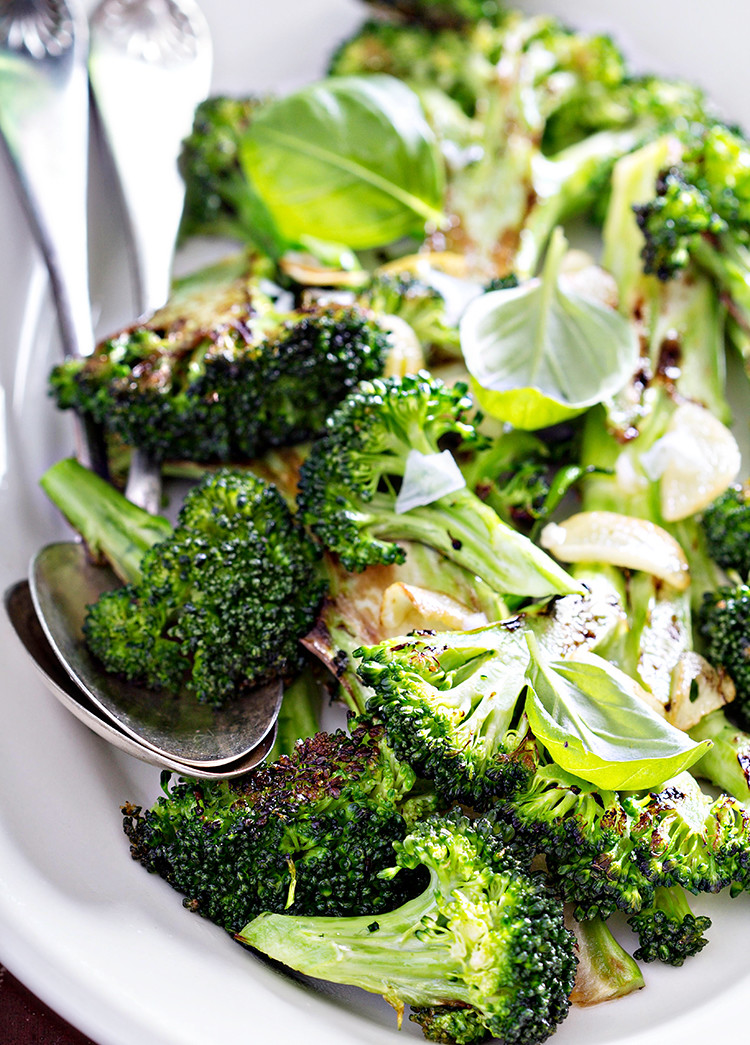 photo of roasted broccoli in a white serving dish with serving spoons