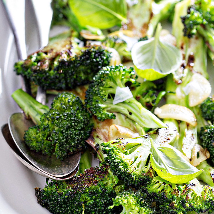 photo of roasted broccoli in a white serving dish with serving spoons