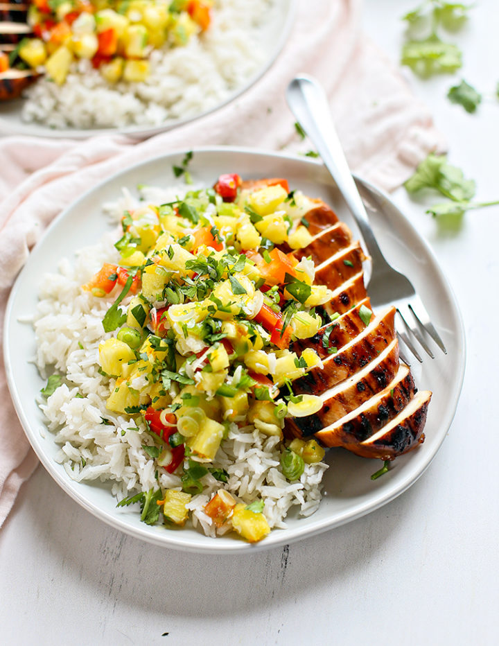 close up photo of a white plate with coconut rice and sliced pineapple salsa chicken