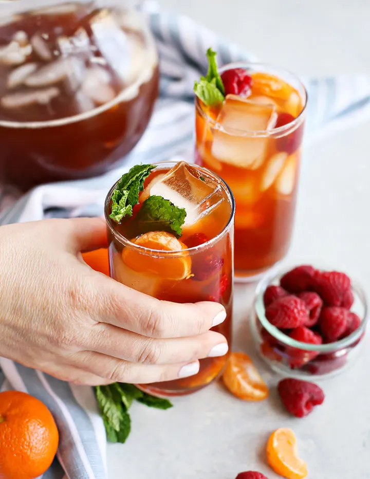 photo of a woman's hand holding a glass of tangerine raspberry iced tea