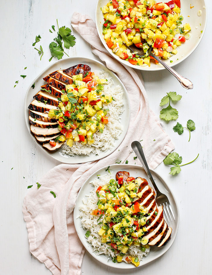 overhead photo of two white plates with coconut rice, pineapple salsa, and pineapple salsa grilled chicken