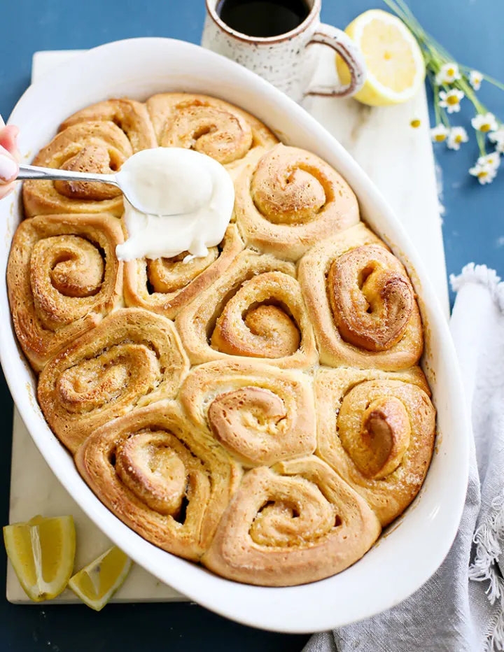 photo of a lemon rolls in a pan being frosted with lemon cream cheese icing