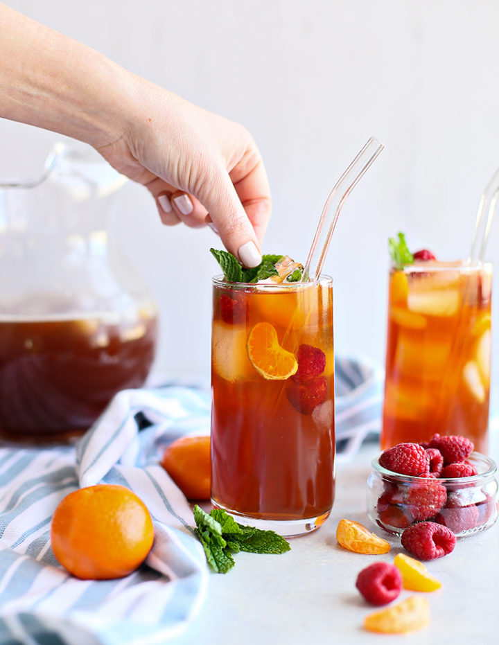 photo of a woman garnishing a glass of raspberry iced tea with fresh mint leaves