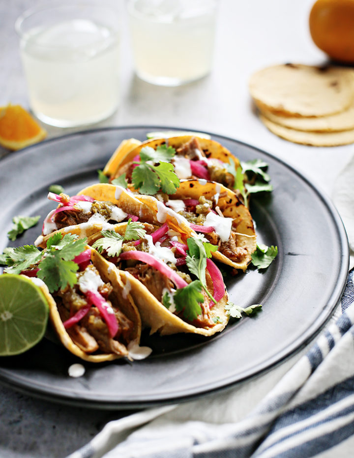 photo of shredded pork tacos on a black plate with cilantro and pickled red onions