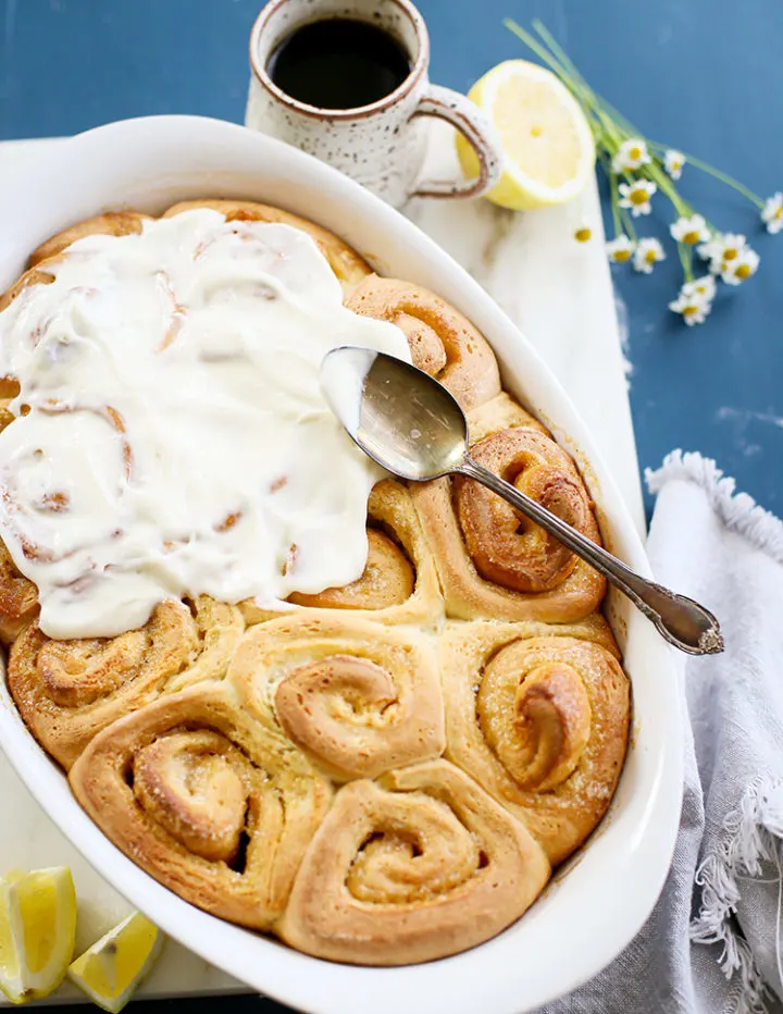 photo of a lemon rolls in a pan being frosted with lemon cream cheese icing