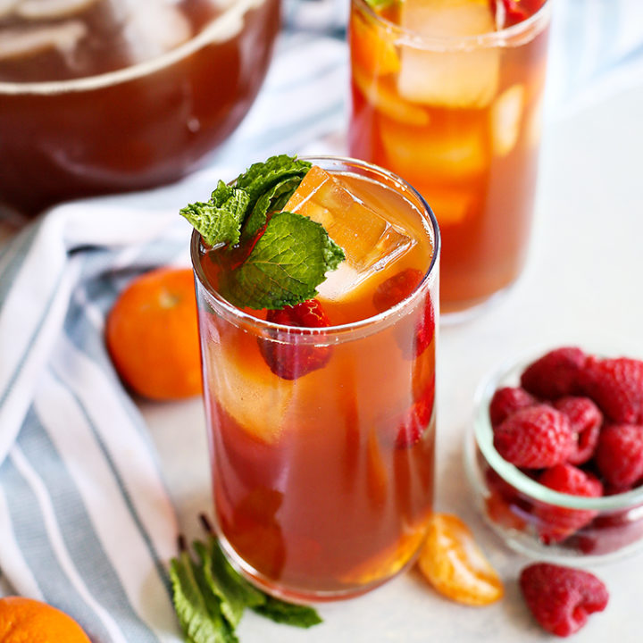 photo of two glasses of raspberry iced tea with a kitchen towel and bowl of raspberries