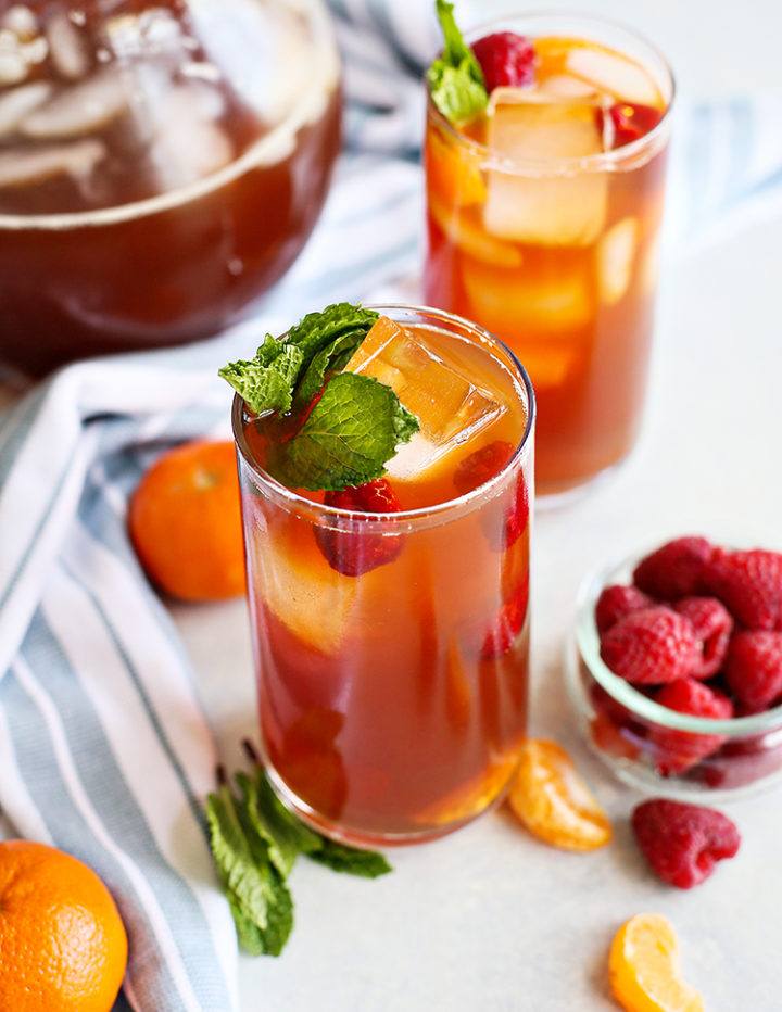 photo of two glasses of tangerine raspberry iced tea with a bowl of raspberries and kitchen towel