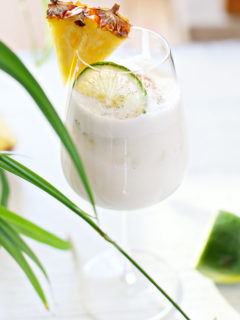 pina colada on the rocks in a glass with a slice of lime and pineapple