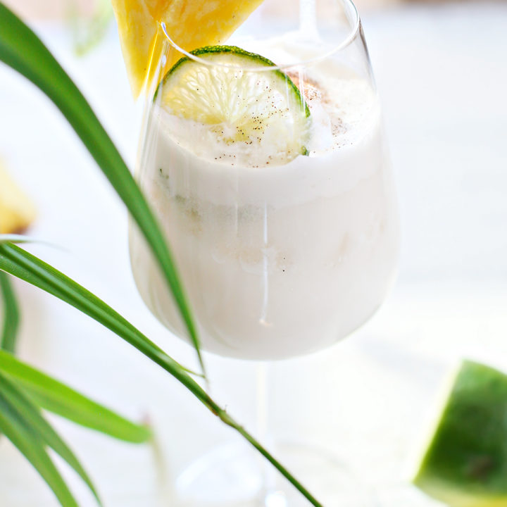 pina colada on the rocks in a glass with a slice of lime and pineapple