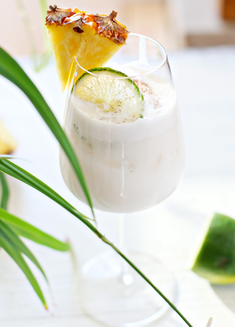 pina colada on the rocks in a glass with a slice of lime and pineapple