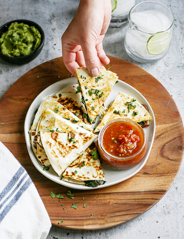 woman holding a slice of a veggie quesadilla over a plate