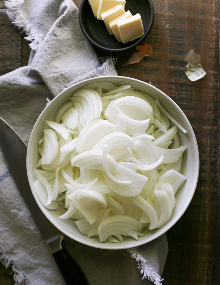 photo of sliced onions in a bowl with a knife and butter