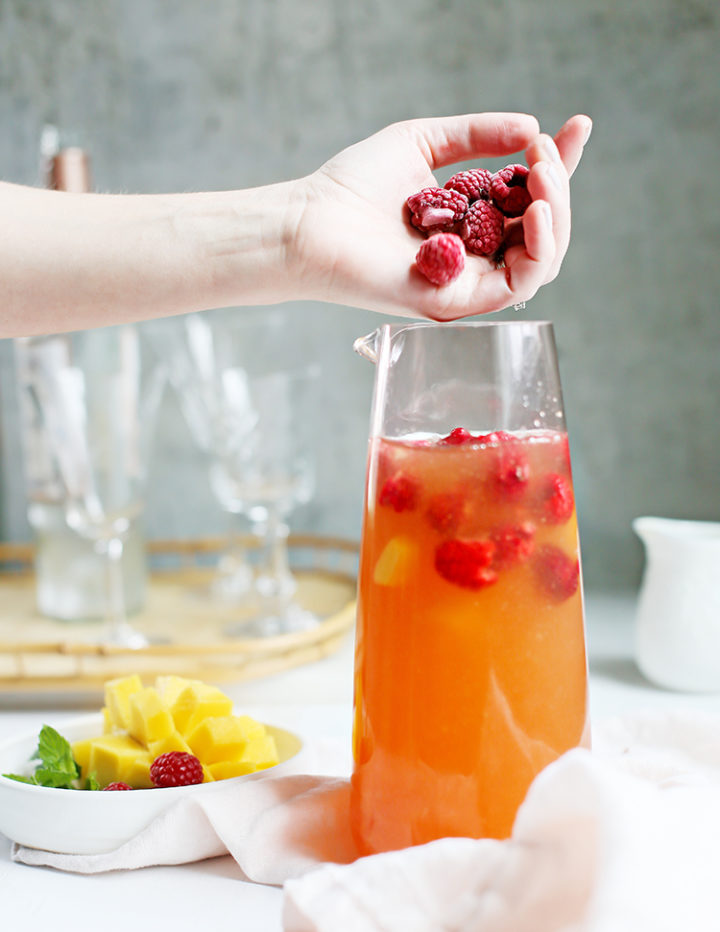 photo of a woman adding raspberries and mango to a pitcher of rosé sangria