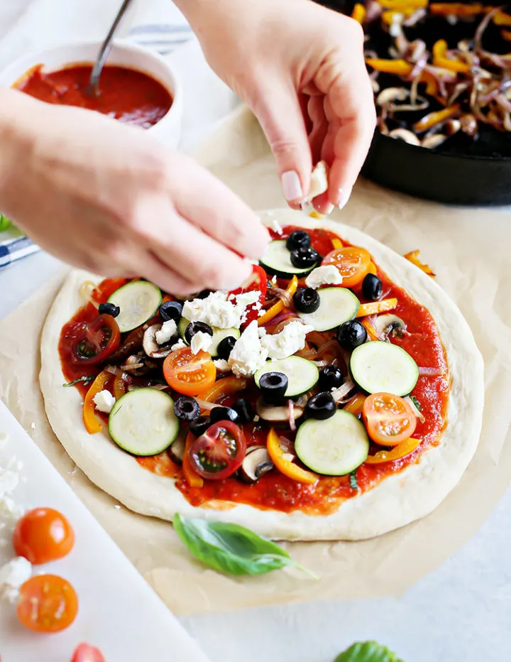 photo of woman putting toppings on a veggie pizza